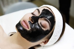 Mujer con mascarilla facial negra de carbón activado en polvo echada en un salón de spá.